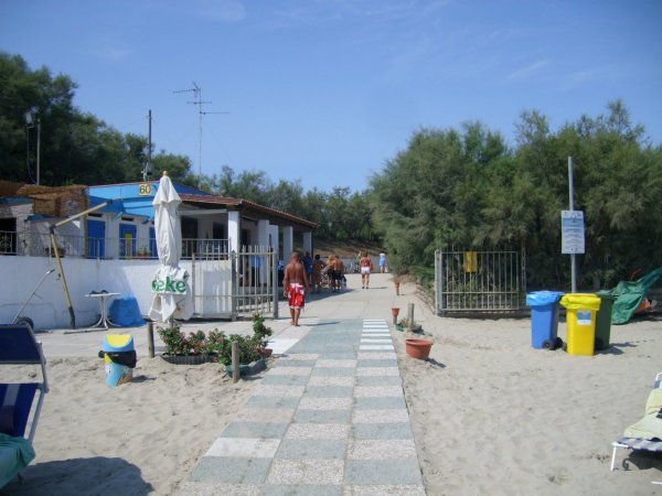 Una passerella su una spiaggia con cabine e bidoni colorati.