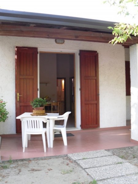 Un patio con tavolo bianco e sedie davanti a una porta con persiane marroni.