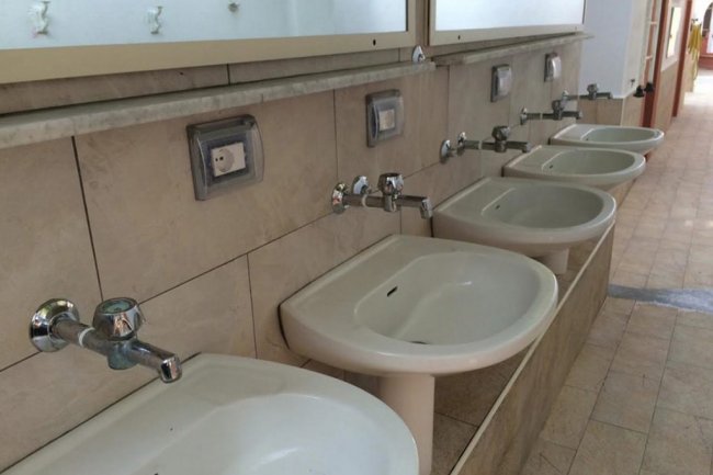 Lavabi bianchi allineati in un bagno con piastrelle beige.