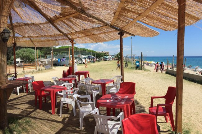Area di ristoro all'aperto con sedie rosse e bianche, vista mare.