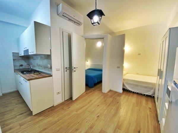 Un appartamento con cucina moderna, pavimento in legno e due stanze arredate.