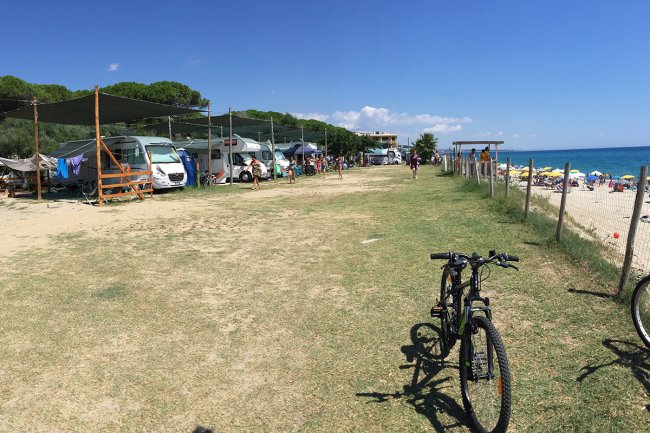 Un'area di campeggio vista mare con camper e bici sul prato.