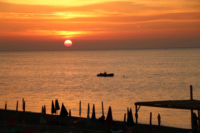Un tramonto sul mare con ombrelloni in silhouette sulla spiaggia.