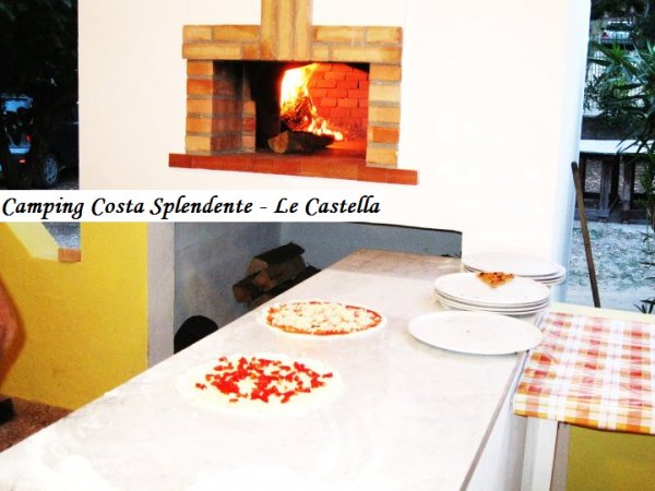 Forno a legna acceso su un piano di lavoro con pizze non cotte e piatti.