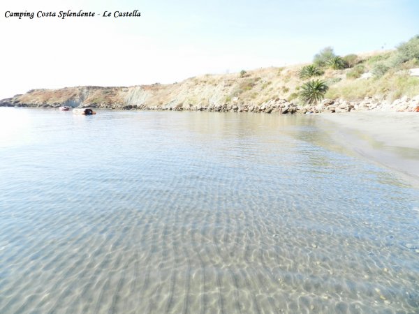 Spiaggia deserta con acqua limpida e colline erbose sullo sfondo.