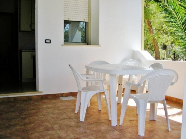 Tavolo e sedie bianche su terrazza pavimentata.