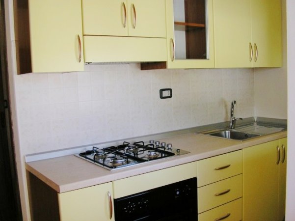 Cucina con mobili gialli, piano cottura e lavello in acciaio.