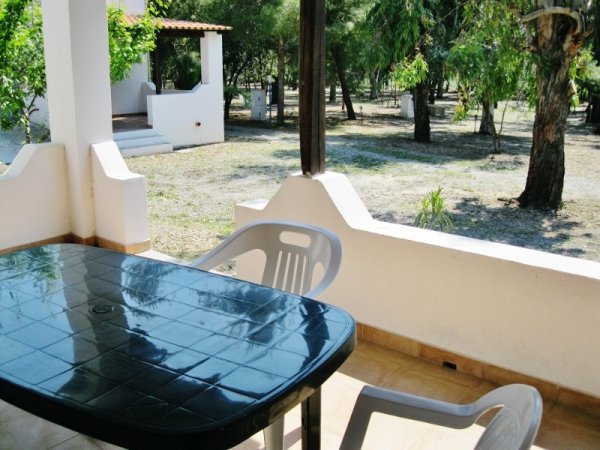 Tavolo nero e sedie su una veranda con vista su un giardino alberato.
