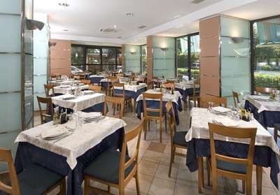 Ristorante con tavoli apparecchiati, sedie di legno e grandi finestre che illuminano l'ambiente.