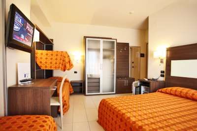 Camera d'hotel con letto matrimoniale, letto a castello, scrivania, TV e armadio bianco.
