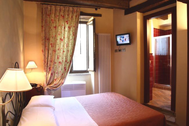 Camera da letto con finestra aperta, tenda fiorita e TV.