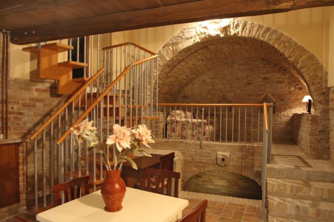 Interno rustico con archi in pietra e scale in legno.