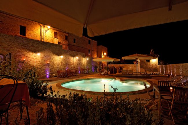 Piscina notturna con ombrelloni e mura in mattoni.