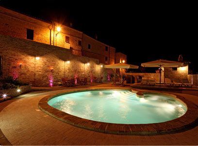 Piscina illuminata di notte accanto a un edificio in mattoni.