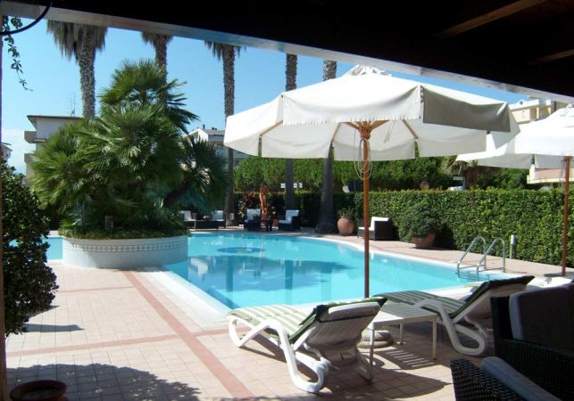 Una piscina con lettini e ombrelloni bianchi, circondata da palme e cespugli.
