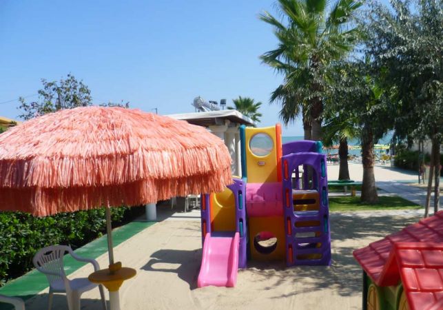 Parco giochi con scivolo colorato e grande ombrellone arancione.