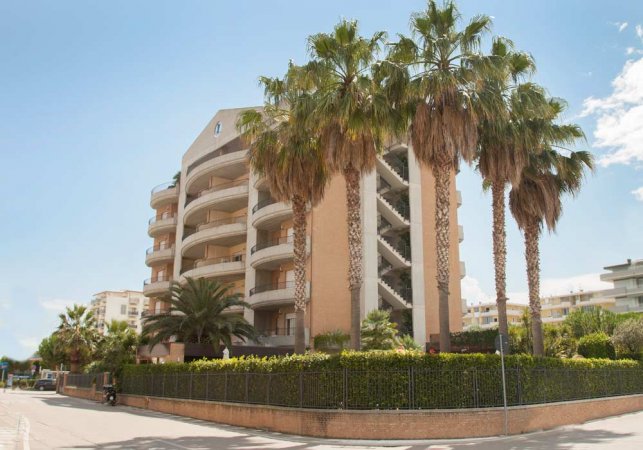 Edificio moderno con balconi curvi e palme.
