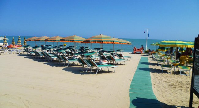 Spiaggia con lettini e ombrelloni colorati, cielo azzurro e mare calmo.