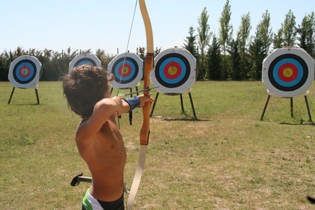 Un bambino mira a un bersaglio con un arco in un campo di tiro con l'arco.