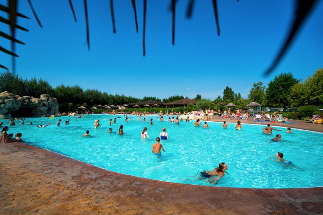 Persone in una grande piscina all'aperto con ombrelloni sullo sfondo.