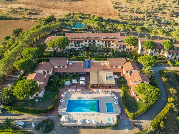 Veduta aerea di un resort con piscina e edifici circondati da alberi e campagna.