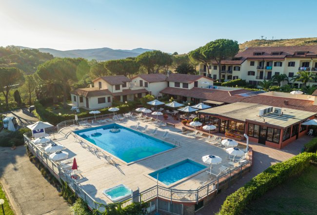 Piscina all'aperto circondata da lettini e ombrelloni, con edifici residenziali sullo sfondo.