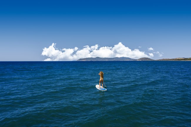 Persona su una tavola da paddle sul mare sotto un cielo azzurro con nuvole bianche.