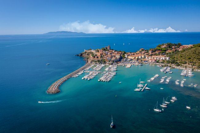 Porto turistico affacciato sul mare con barche ormeggiate e un borgo sulla costa.