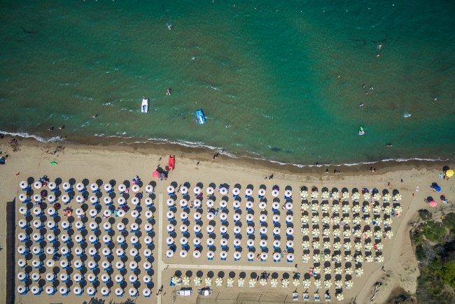 Spiaggia affollata con file di ombrelloni colorati e persone in acqua.