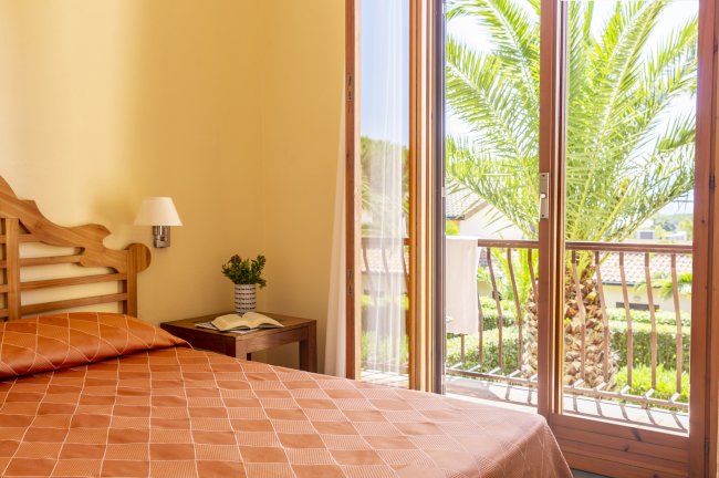 Camera da letto con letto matrimoniale, finestra con vista su palme e balcone.
