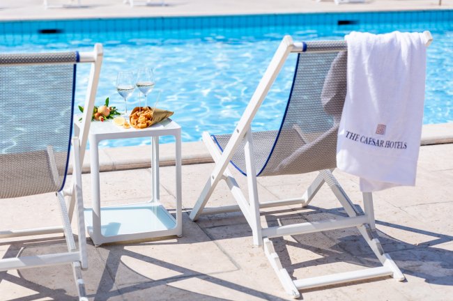 Due sedie a sdraio vicino a una piscina con accanto un tavolino con vino e snack.