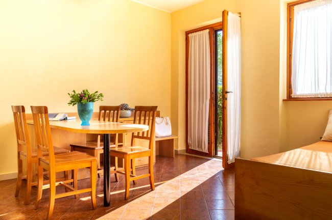Sala luminosa con tavolo in legno, sedie, portafiori e porta aperta.
