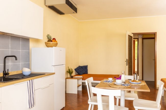 Cucina moderna con tavolo apparecchiato. Pareti chiare, frigorifero bianco e sedie bianche.