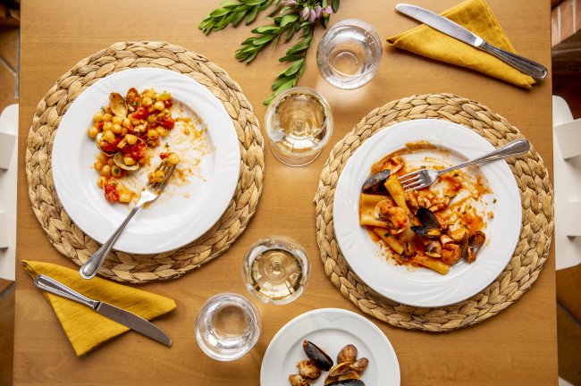 Due piatti di pasta con frutti di mare su una tavola apparecchiata. Bicchieri e posate visibili.