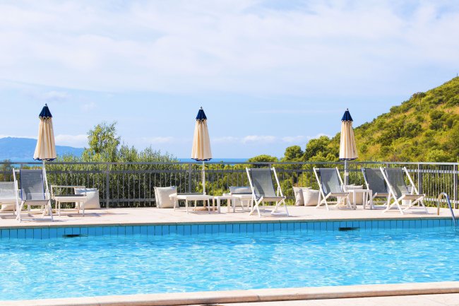 Una piscina all'aperto con sedie a sdraio e ombrelloni gialli, con colline verdi sullo sfondo.