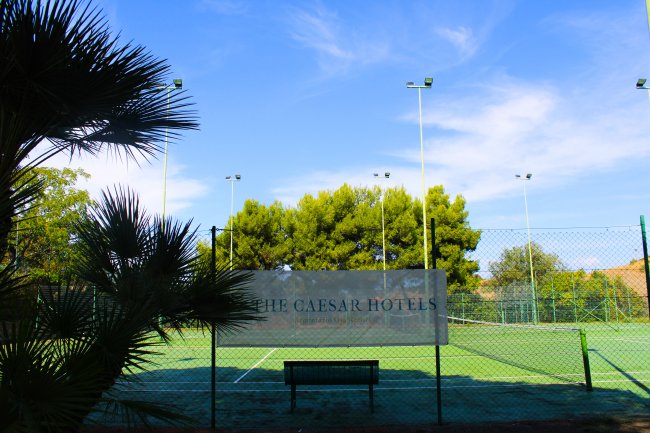 Campo da tennis con rete e cartello, alberi sullo sfondo.