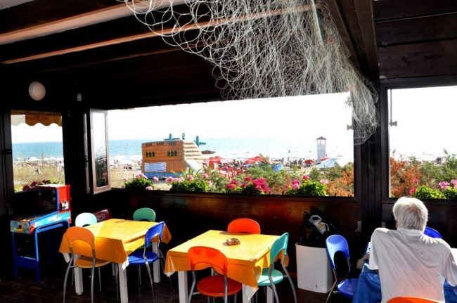 Terrazza con tavoli colorati che si affaccia sul mare e un'area giochi gonfiabile.