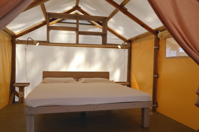 Roulotte con letto matrimoniale e tende arancioni in una struttura in legno.