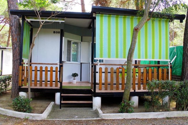 Piccolo bungalow con veranda e tende verdi a righe.