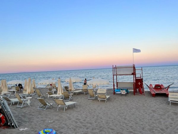 Spiaggia con lettini, ombrelloni chiusi e torre di salvataggio.