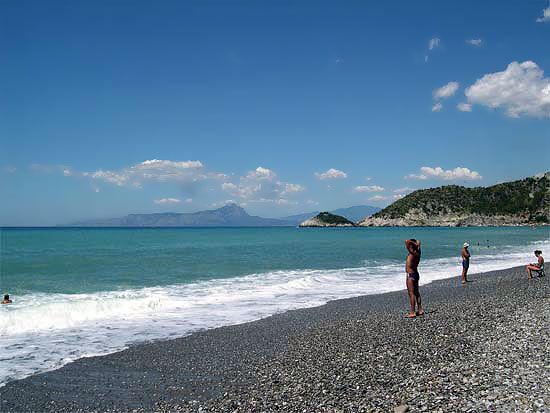 Spiaggia di ciottoli con bagnanti e mare calmo, cielo sereno con poche nuvole.
