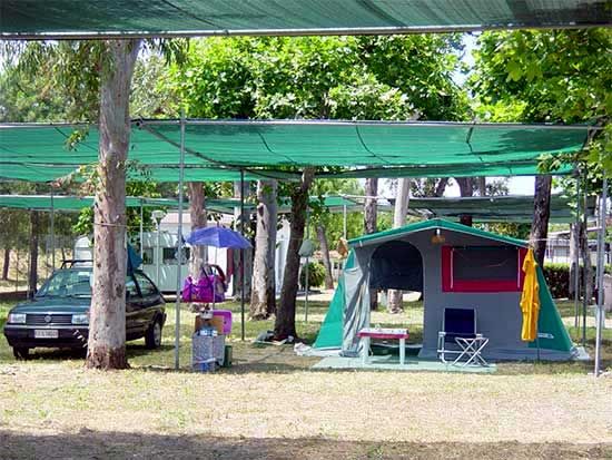 Una tenda verde con ombrellone e sedie sotto alberi ombreggiati vicino a un'auto.