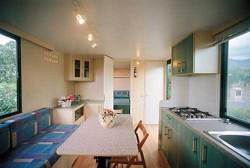 Interno di una casa mobile con cucina, tavolo, divano e finestre luminose.