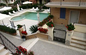 Piscina con lettini e ombrelloni in un cortile ben curato, adornato da fiori rossi.