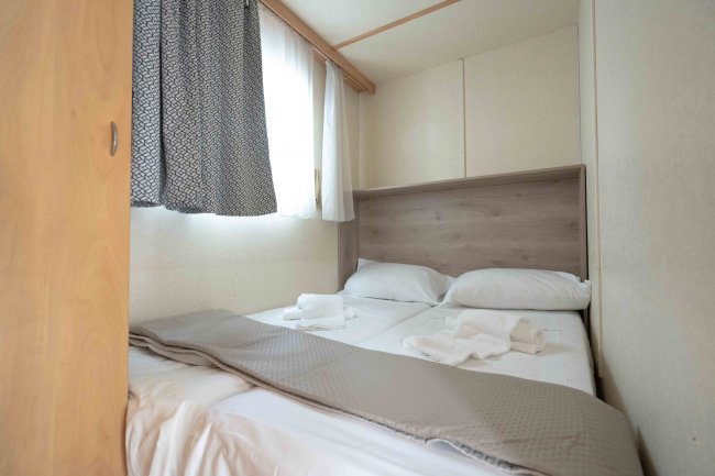 Camera con letto matrimoniale, lenzuola bianche, tende e una finestra luminosa.