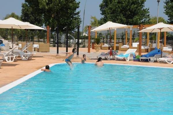 Piscina all'aperto con persone che nuotano, circondata da lettini e ombrelloni.