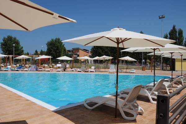 Piscina all'aperto con sedie a sdraio e ombrelloni bianchi.