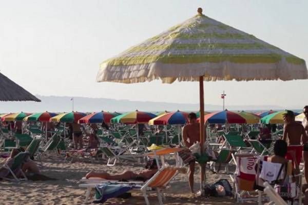 Spiaggia affollata con ombrelloni colorati e persone sdraiate sui lettini sotto il sole.