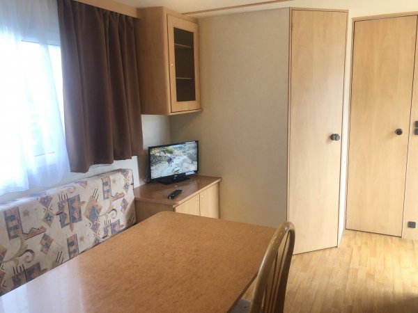 Interno di una stanza con tavolo in legno, televisore su mobile e divano con motivo geometrico.