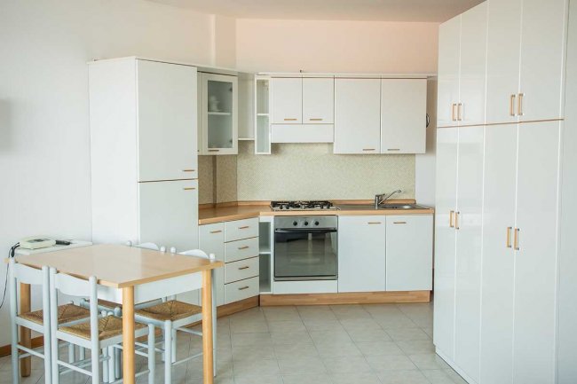 Cucina moderna bianca con forno e tavolo.